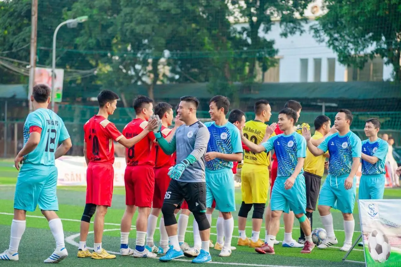 Two soccer teams shake hands on the field in Hanoi, showcasing sportsmanship.