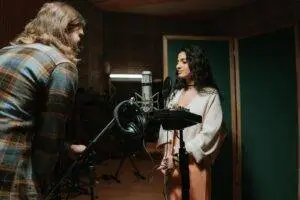 A woman recording vocals in a professional music studio setting.