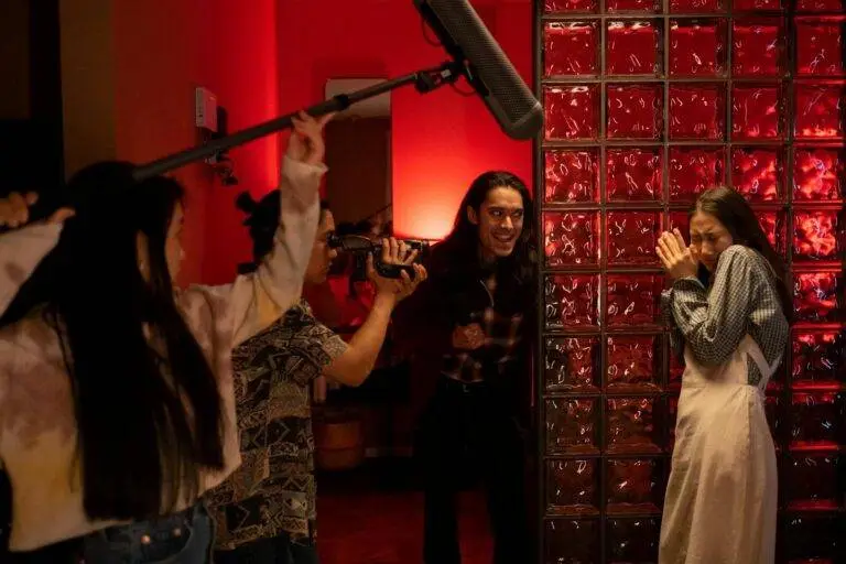 A group of teenagers filming a playful horror scene indoors with a boom mic and camera.